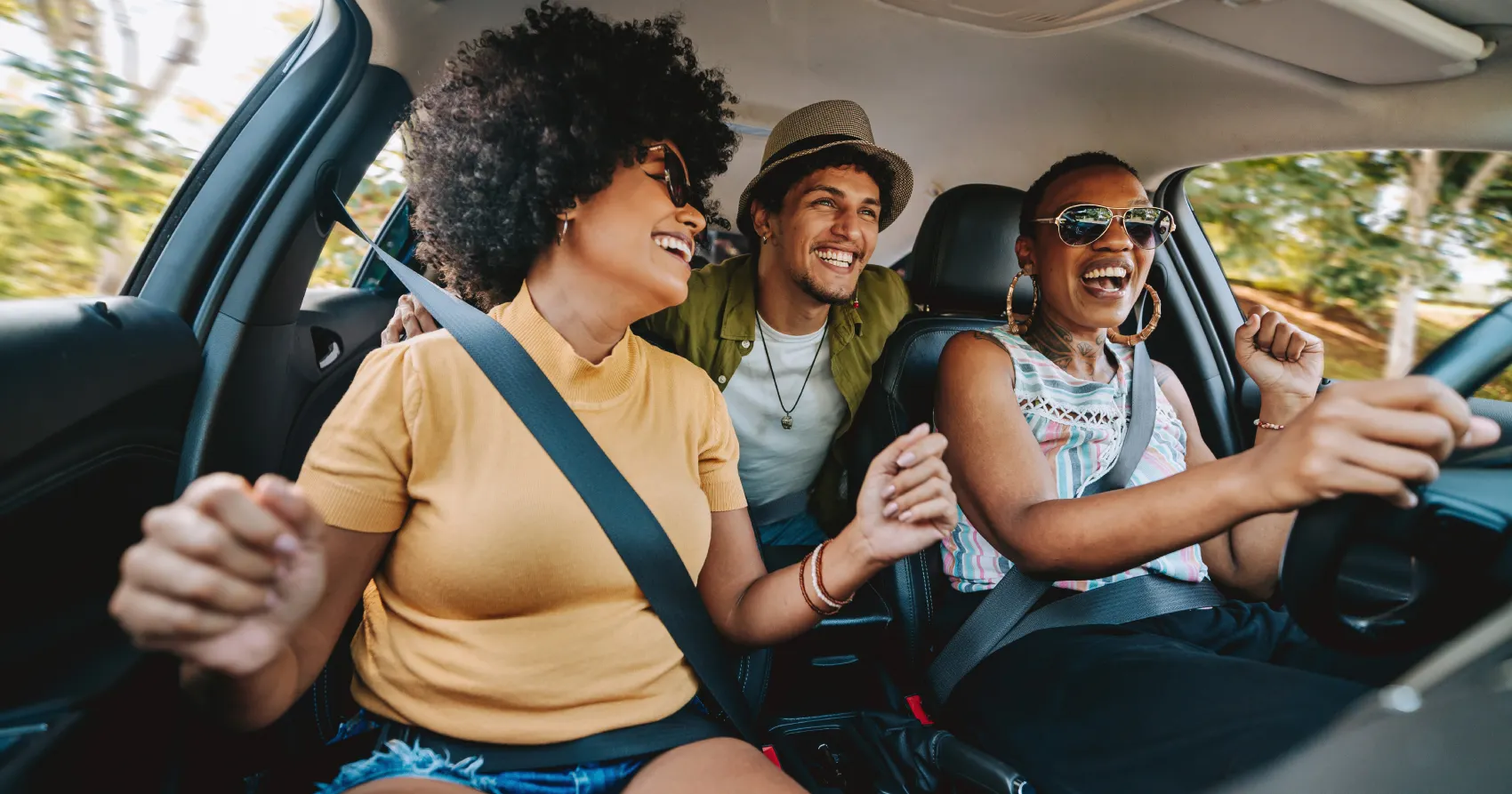 Três amigos sorrindo e rindo dentro de um carro alugado, aproveitando a viagem no exterior.