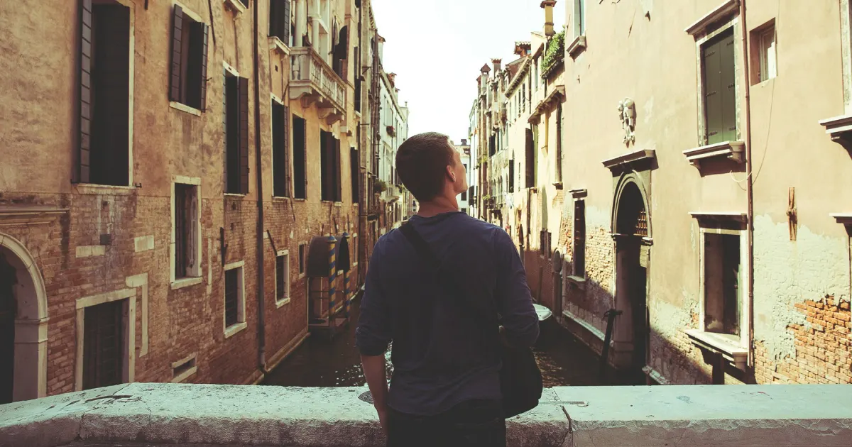 Homem de costas em uma ponte de cidade europeia observando a paisagem medieval
