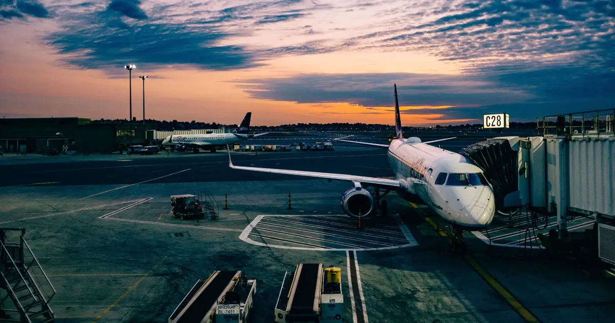 Imagem de um avião parado em um aeroporto com uma ponte de embarque acoplada.