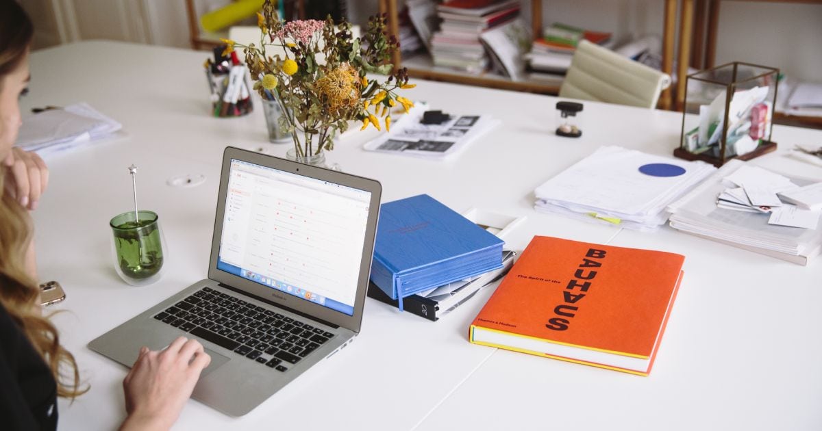 mulher utilizando notebook ao lado de um livro laranja