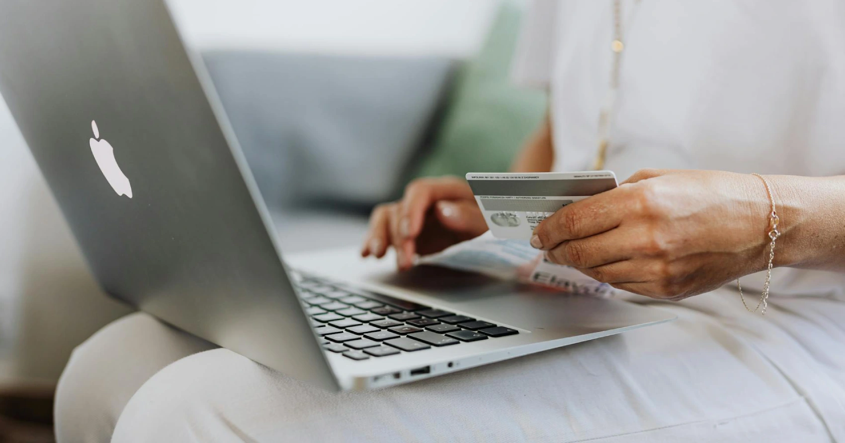 Mulher com um laptop no colo e segurando um cartão de crédito