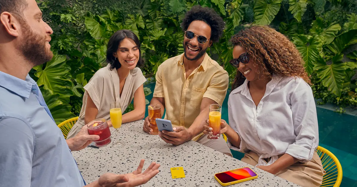 Grupo de amigos usando celular sentados à uma mesa em meio a um jardim