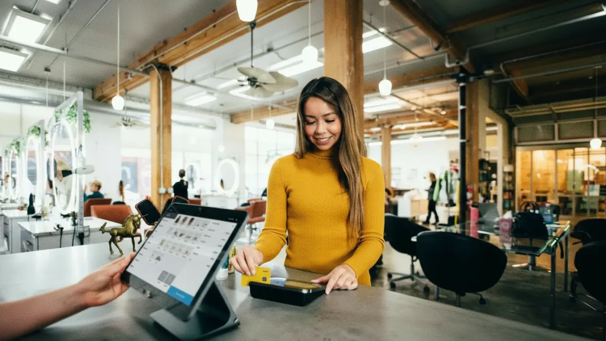 Mulher sorridente realizando pagamento com cartão de débito amarelo da Nomad em uma máquina de cartão dentro de um estabelecimento comercial moderno.