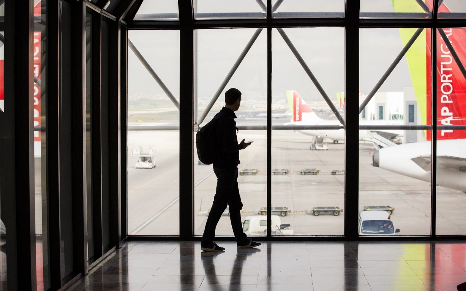 Silhueta de pessoa observando aviões por uma janela em um aeroporto