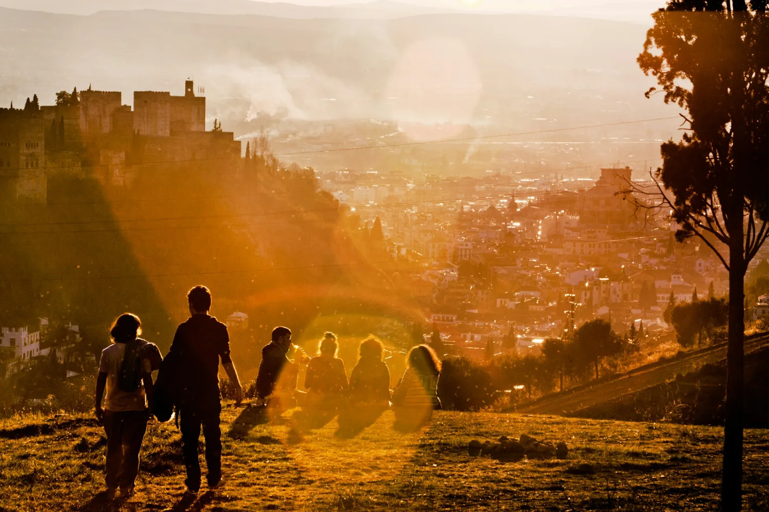 Grupo de pessoas sentadas em campo com grama observando a Alhambra, em Granada, durante o pôr do sol