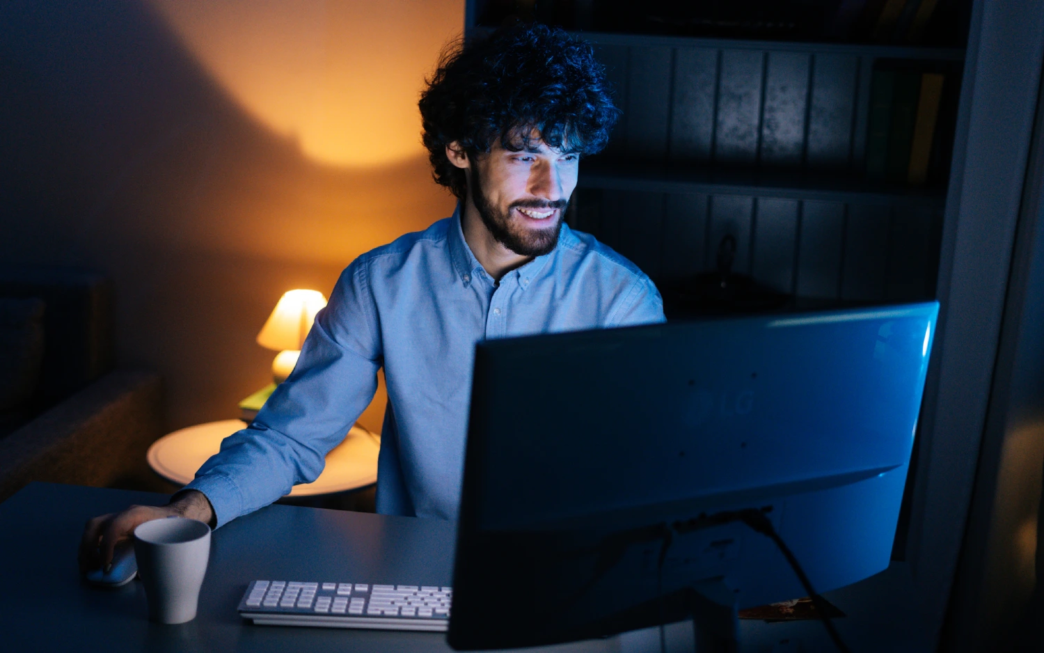 Homem branco com cabelo ondulado sentado à escrivaninha usando um computador