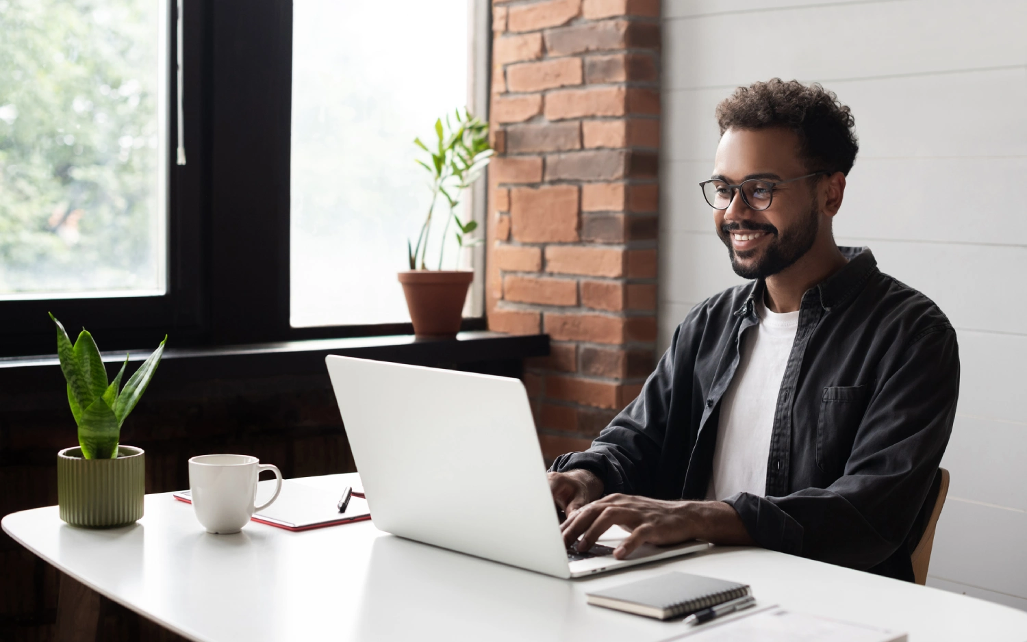 Homem negro de camiseta branca e camisa xadrez escura usando notebook