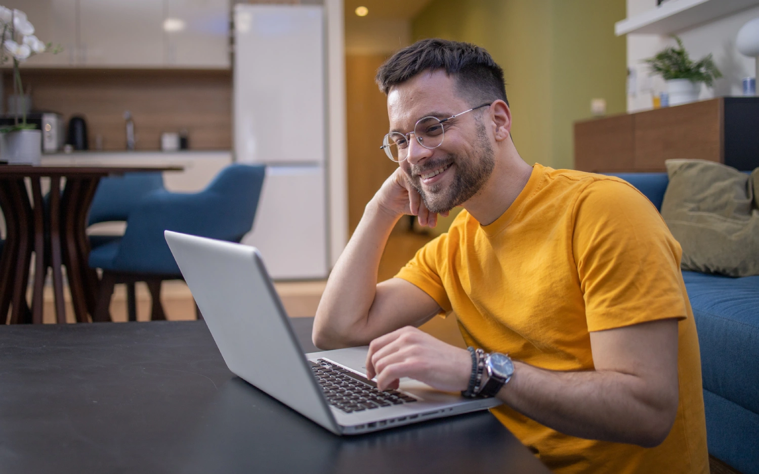 Homem de camisa amarela e óculos usando notebook
