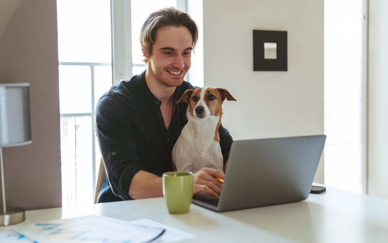 Homem segurando cachorro usando um notebook em ambiente iluminado