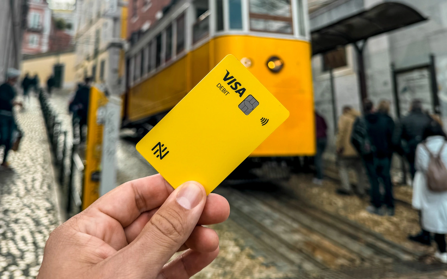 Pessoa segurando cartão de débito amarelo com bonde de Lisboa ao fundo