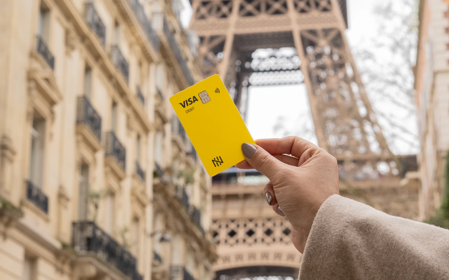 Close em mão segurando Cartão de Débito Internacional Nomad com Torre Eiffel ao fundo