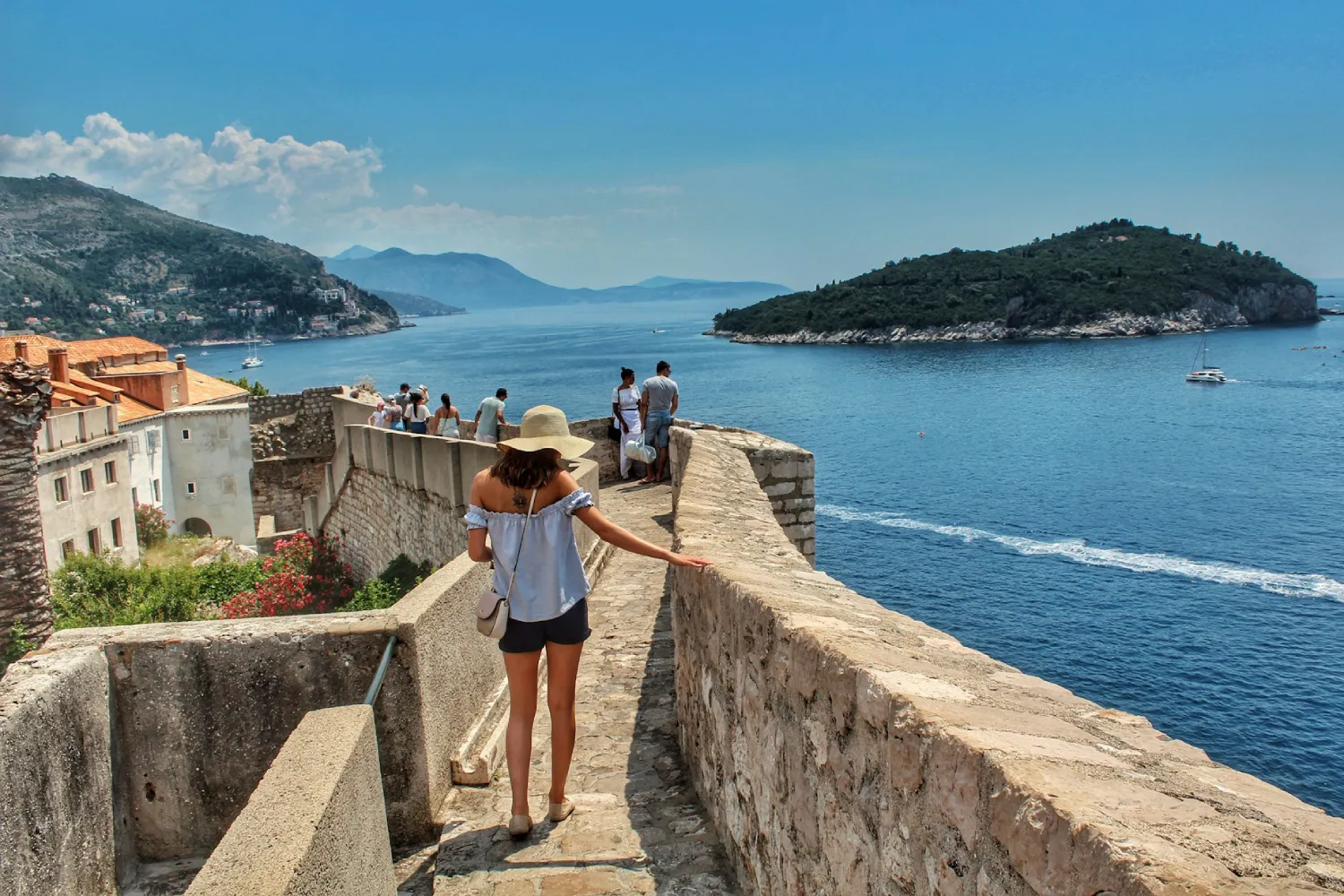 Mulher com camisa branca e chapéu caminhando pela Muralha de Dubrovnik