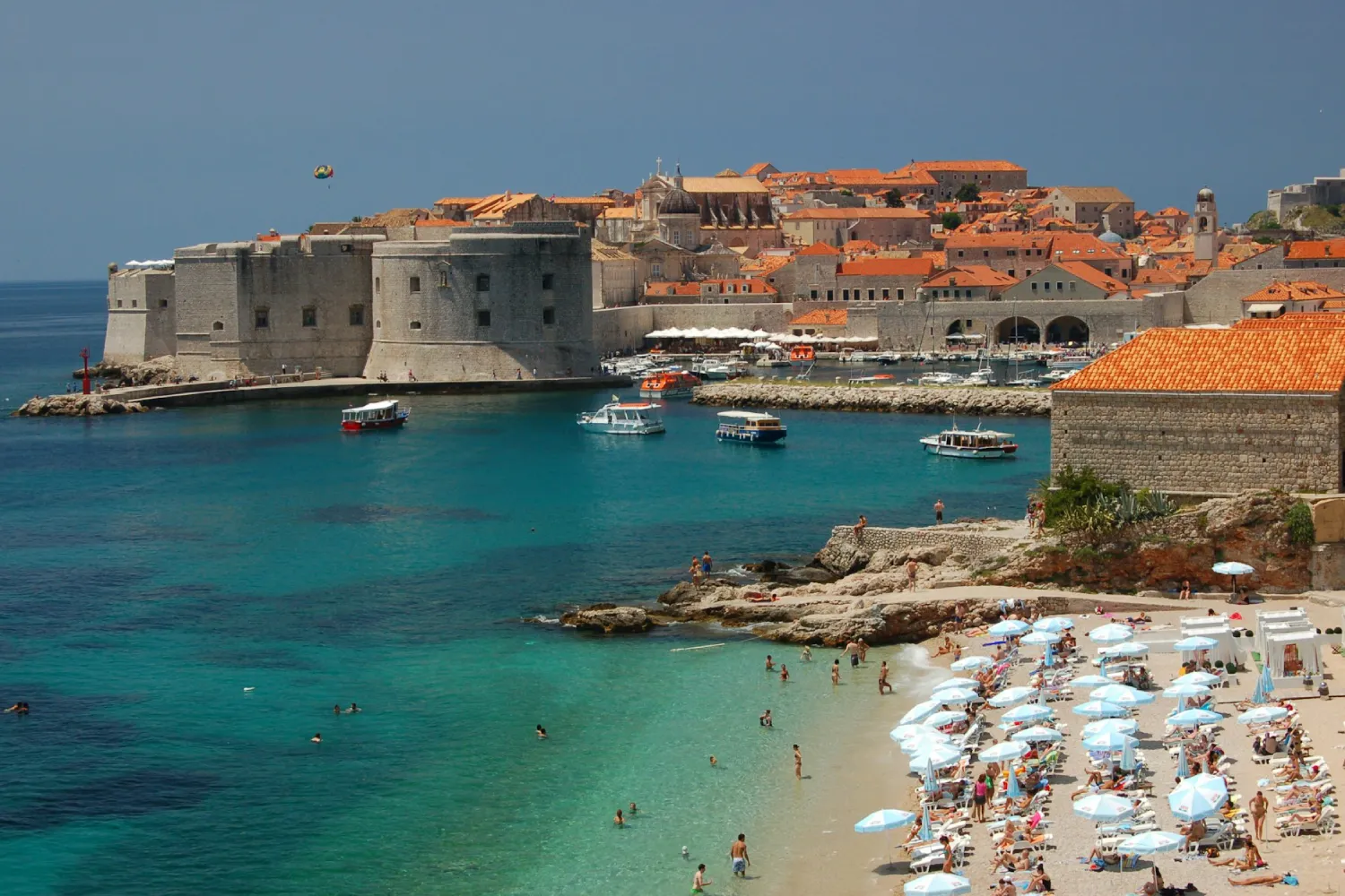 Banhistas em praia de Dubrovnik com o Forte de São João e a Cidade Antiga ao fundo