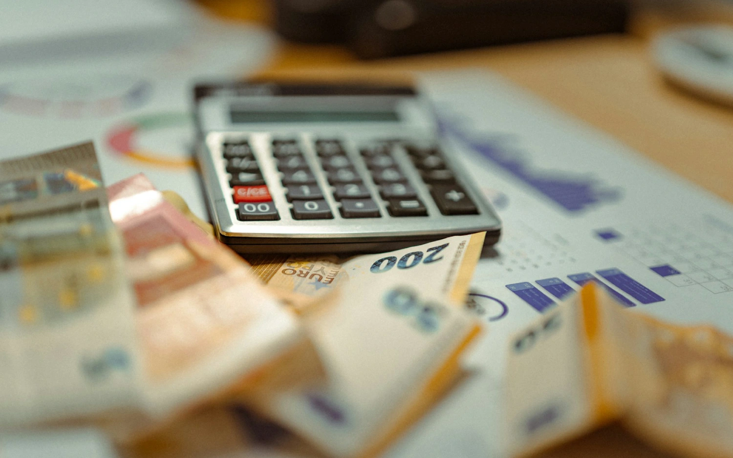 Calculadora com notas de dinheiro e folhas de papel espalhadas sobre uma mesa