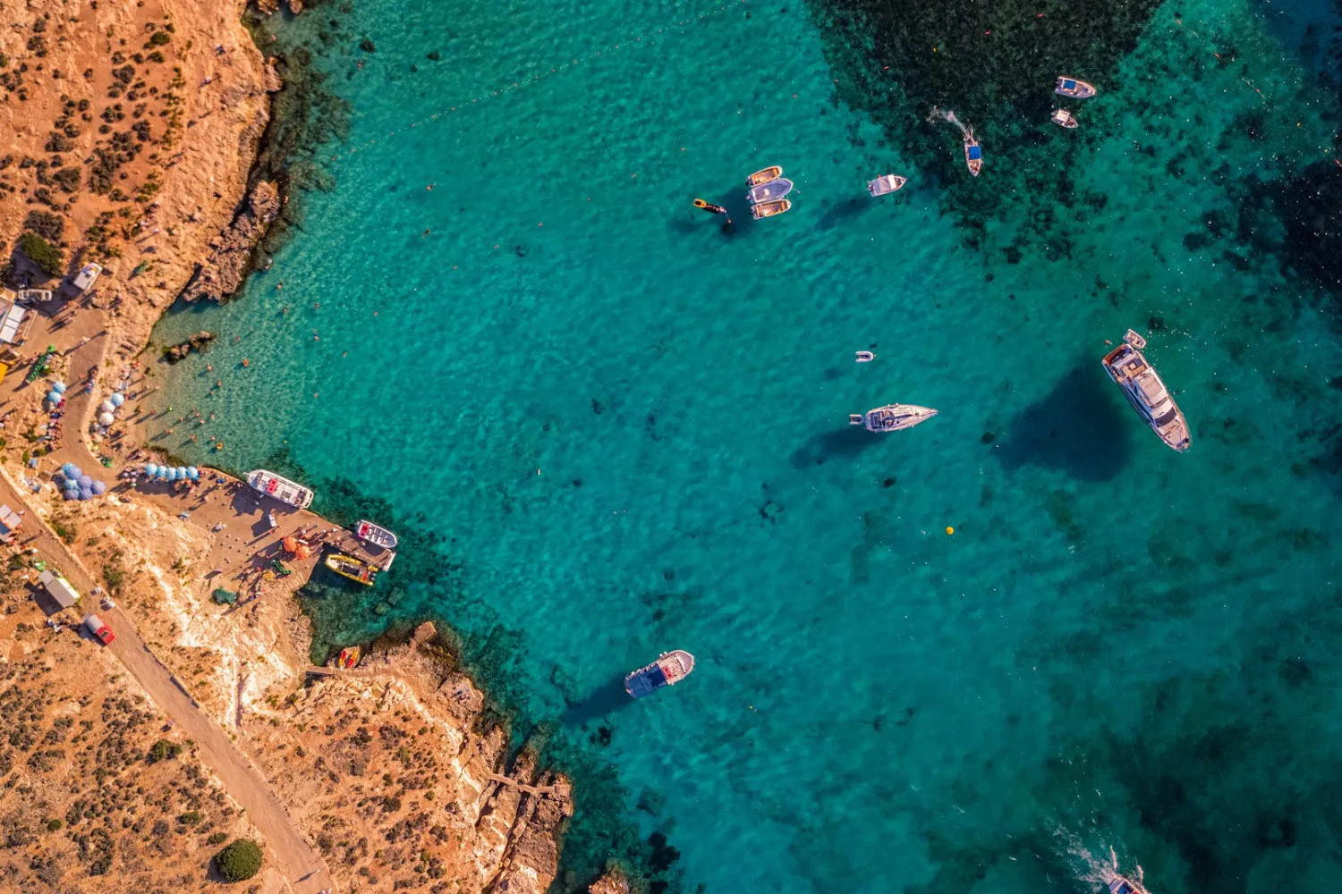 Visão aérea do Blue Lagoon, em Malta, com águas azul-turquesa, banhistas e embarcações
