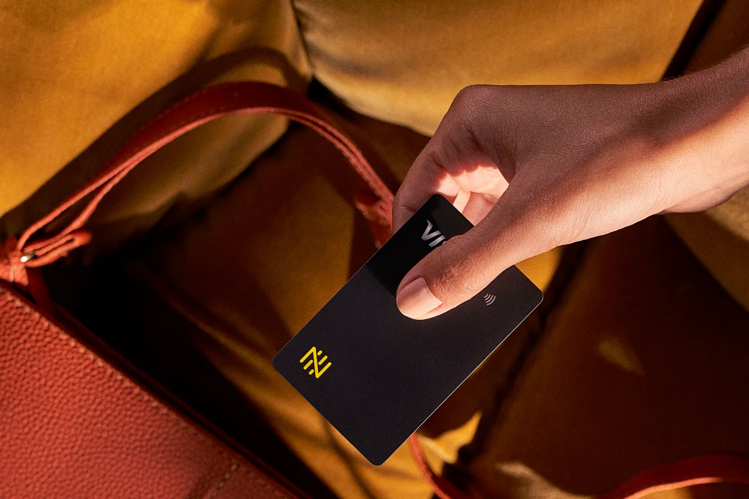Imagem em detalhe de mão retirando o Cartão de Débito Internacional Nomad de uma bolsa