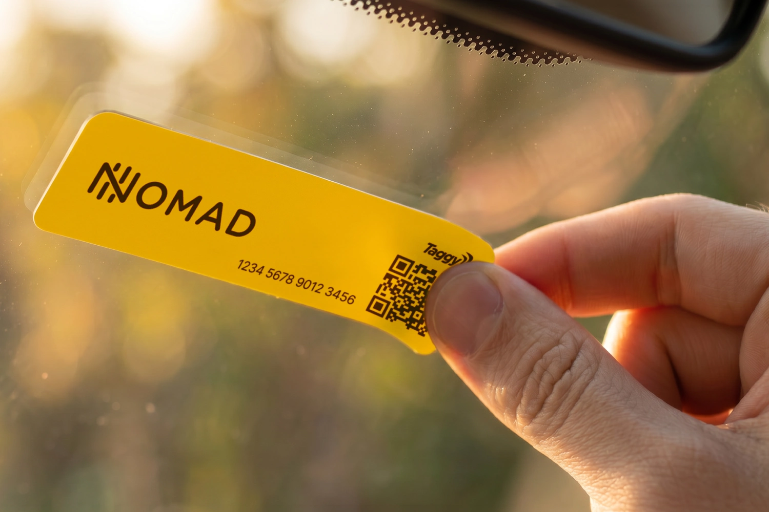 Detalhe de mão colando a Nomad Tag no vidro de um carro