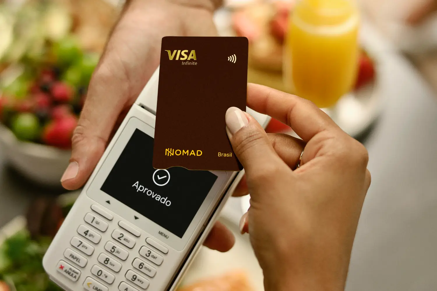 Detalhe de pessoa segurando o Cartão de Débito Internacional Nomad e fazendo um pagamento em uma maquininha