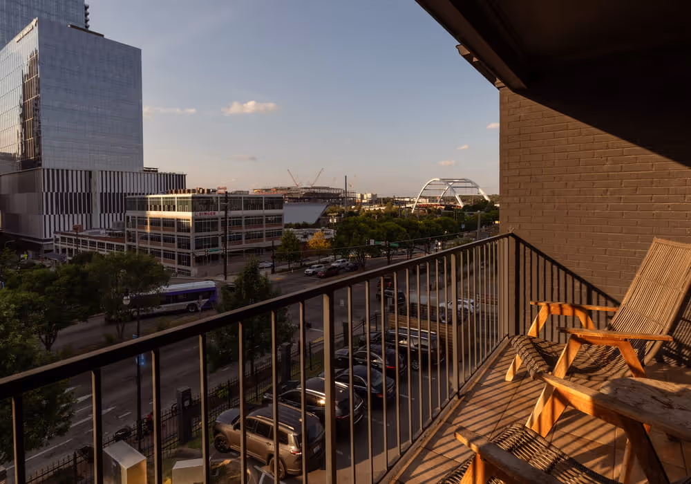 City skyline view from apartment balcony with wooden chairs, arch bridge, and modern buildings at golden hour