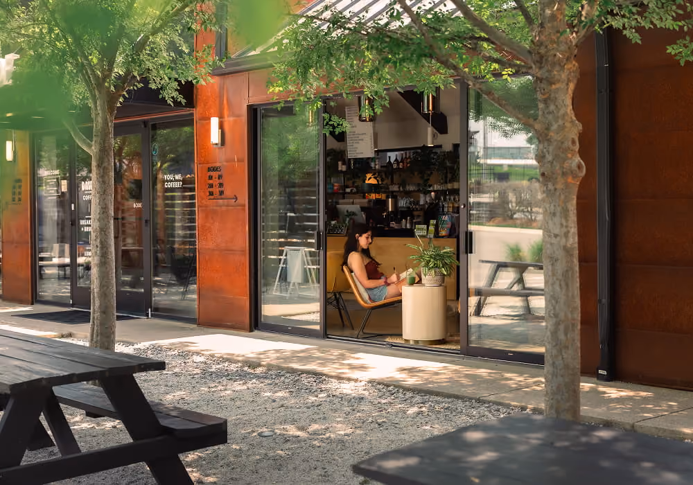 Guest relaxing with coffee in the lobby café at Bode Nashville, seen from the tree-shaded courtyard with picnic tables