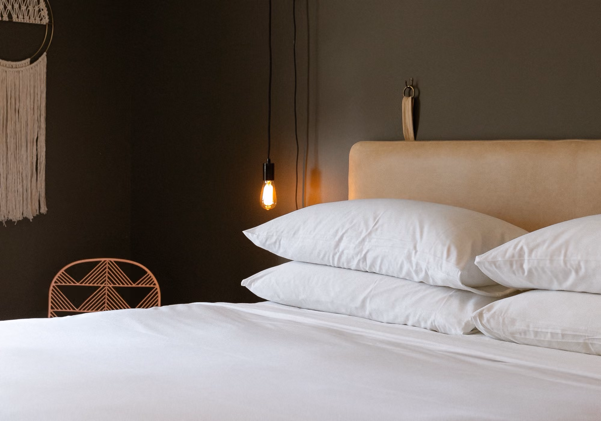 King bed with white linens, leather headboard and hanging Edison bulb in a two-bedroom premium suite