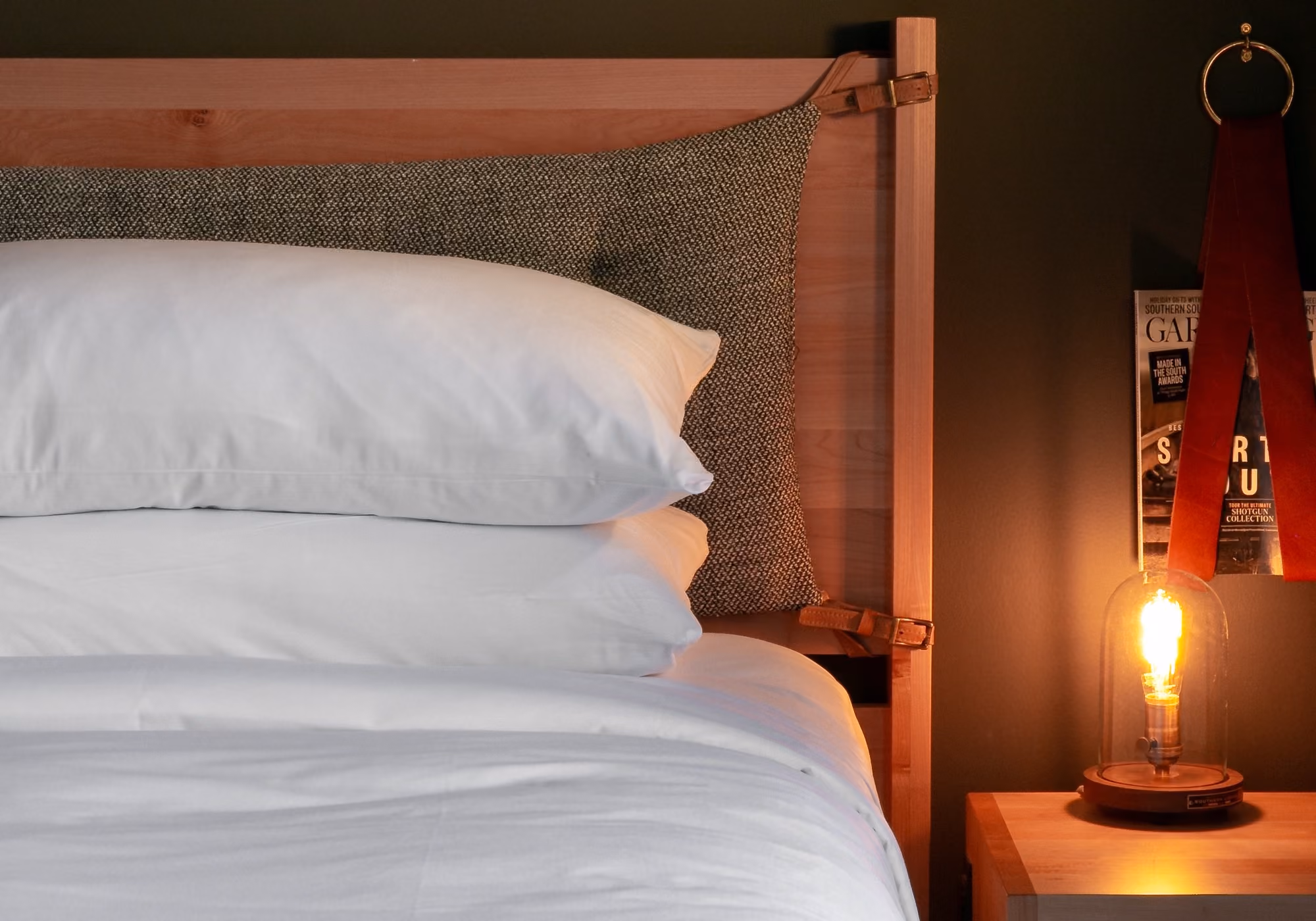 Bed with tweed headboard cushion, magazine rack and Edison bell jar lamp in a three-bedroom suite