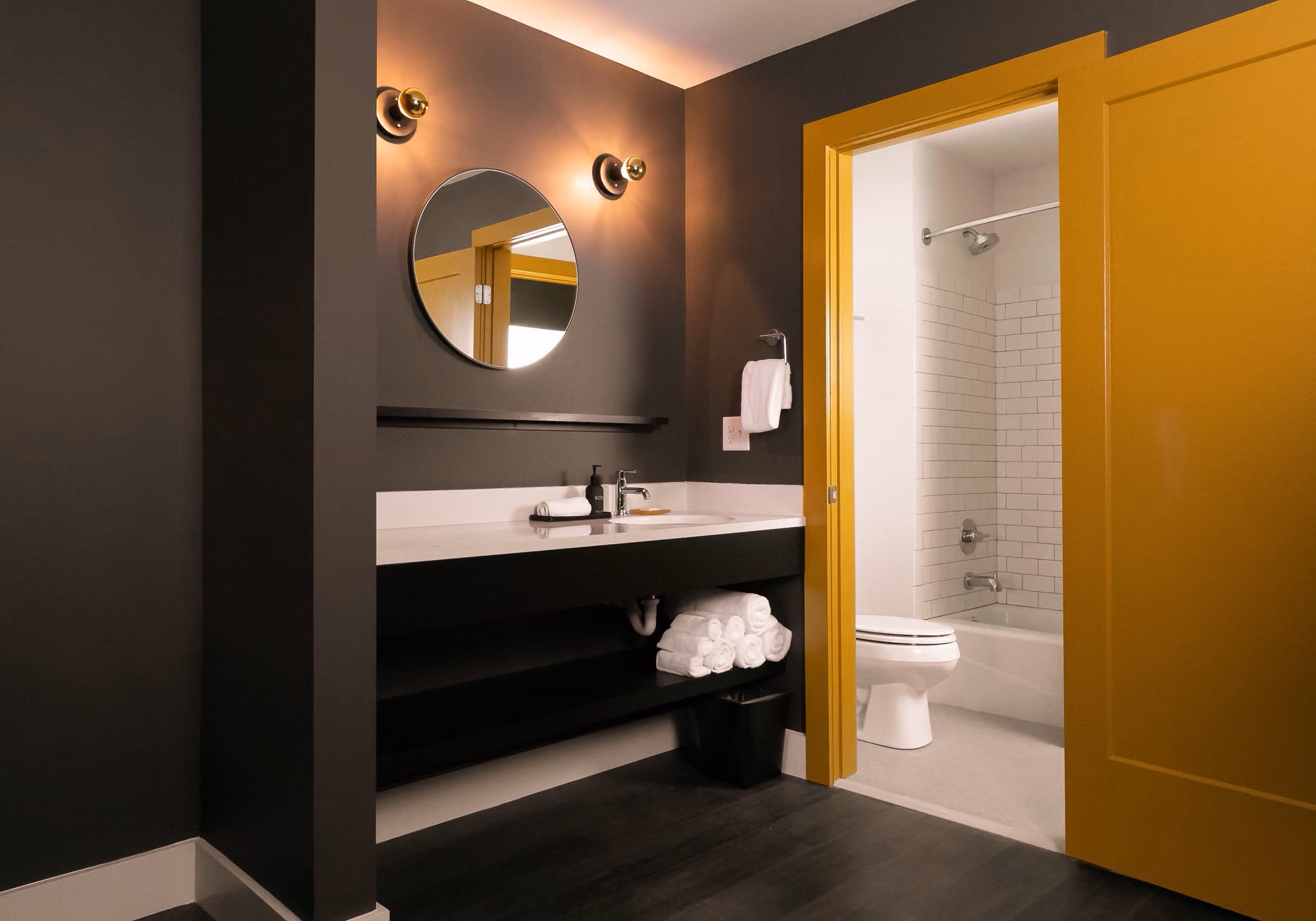 Bathroom with round mirror, white vanity and yellow sliding door to the tub in a three-bedroom suite