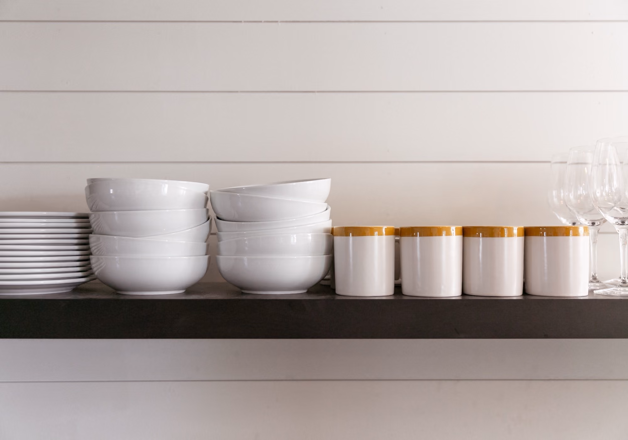 Open kitchen shelf with white plates, bowls, mugs and wine glasses in a four-bedroom suite