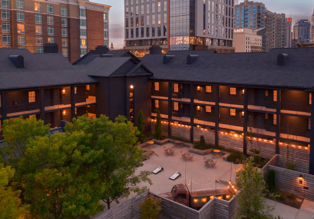Dark-painted boutique hotel courtyard with string lights, outdoor seating, and cornhole boards at dusk in a downtown city