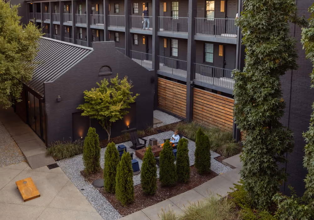 Aerial view of a landscaped courtyard with evergreen trees and seating area between dark brick apartment buildings