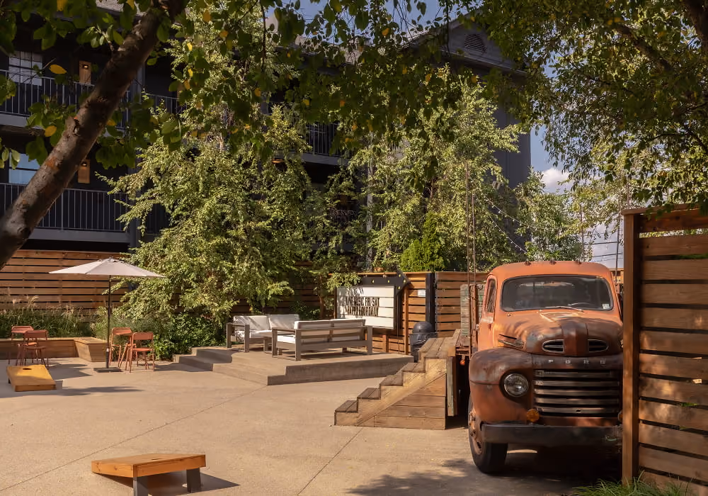 Charming hotel courtyard with a vintage rusty Ford truck, string lights, lounge seating, and cornhole boards under leafy