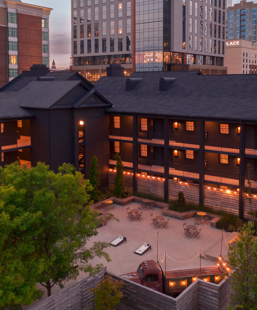 Aerial view of the Bode Nashville courtyard at dusk with string lights, lounge seating, and the downtown Nashville skyline
