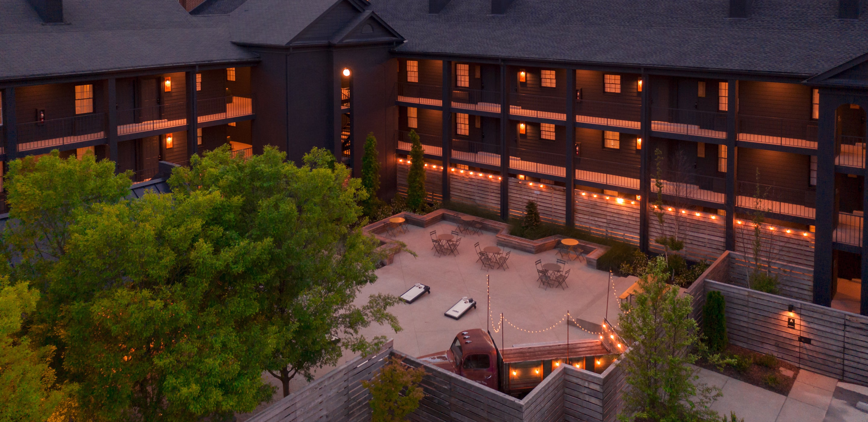 Aerial view of the Bode Nashville courtyard at dusk with string lights, lounge seating, and the downtown Nashville skyline
