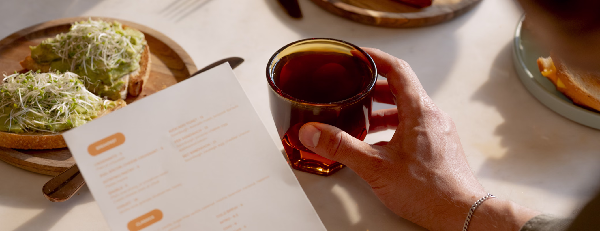 Guest holding a Dawn cafe menu and a glass of iced tea next to avocado toast
