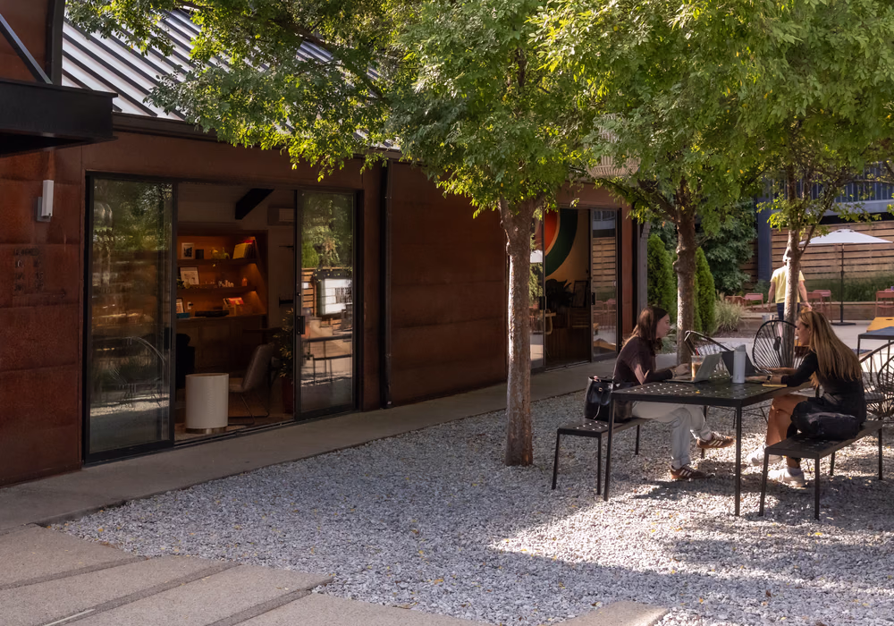 Guests relaxing at patio tables under the trees outside Dawn cafe in the Bode Nashville courtyard