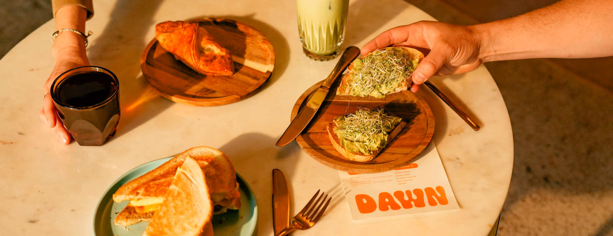 Breakfast at Dawn cafe with avocado toast, croissant sandwich, coffee, and iced matcha latte on a marble table
