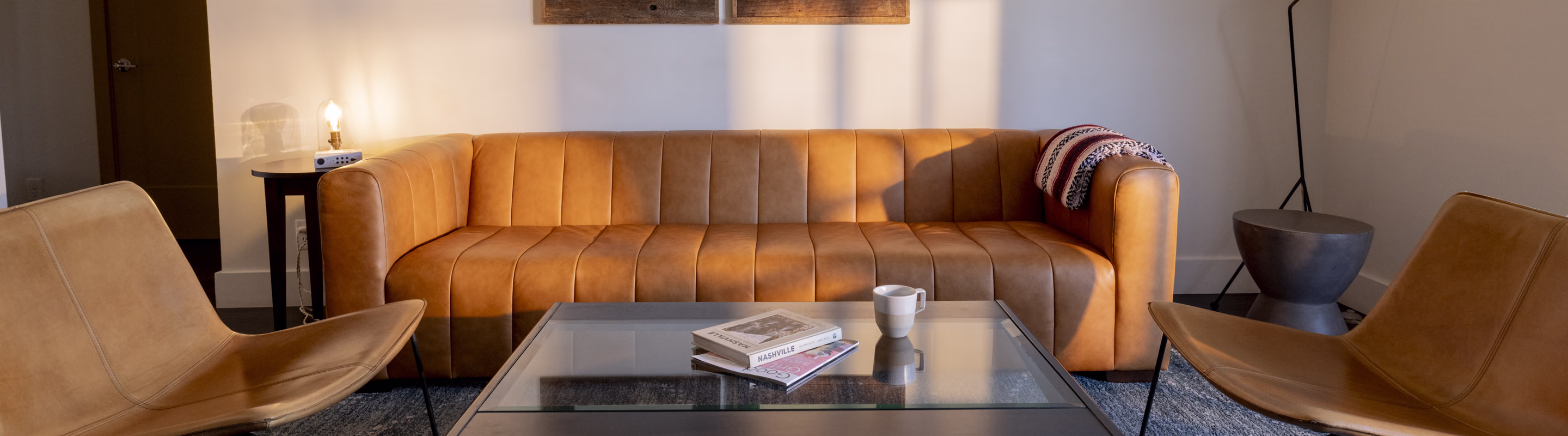 Bode Nashville suite living room with a leather sofa and lounge chairs in afternoon light