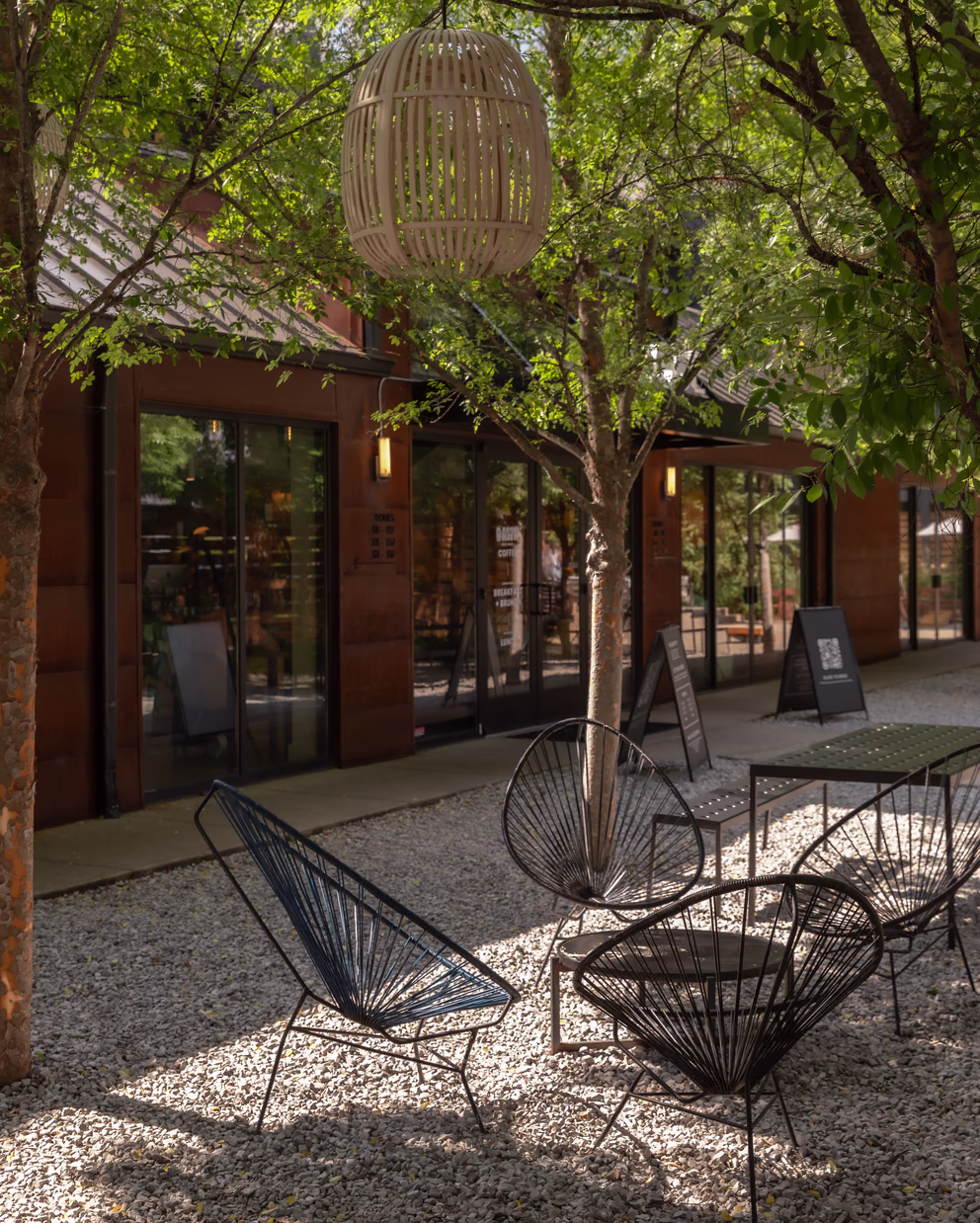 Shaded Bode Nashville courtyard with woven lounge chairs, trees, and a rattan pendant lantern