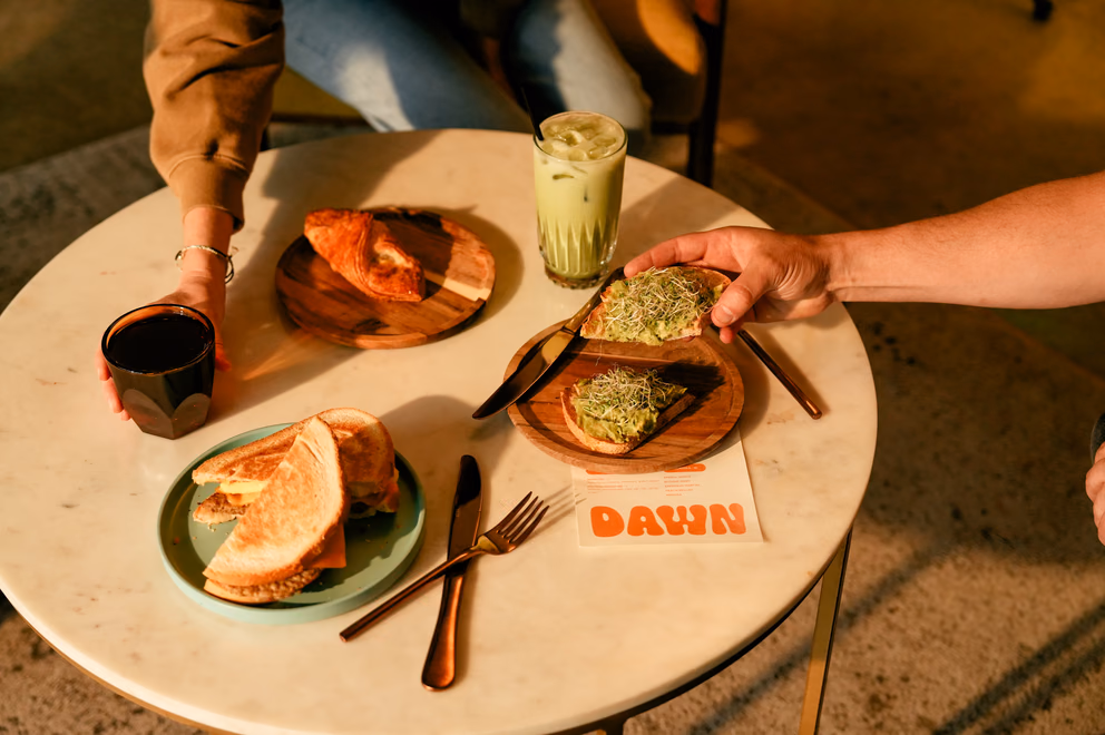 Friends sharing avocado toast, a croissant sandwich, and an iced matcha latte at Dawn cafe