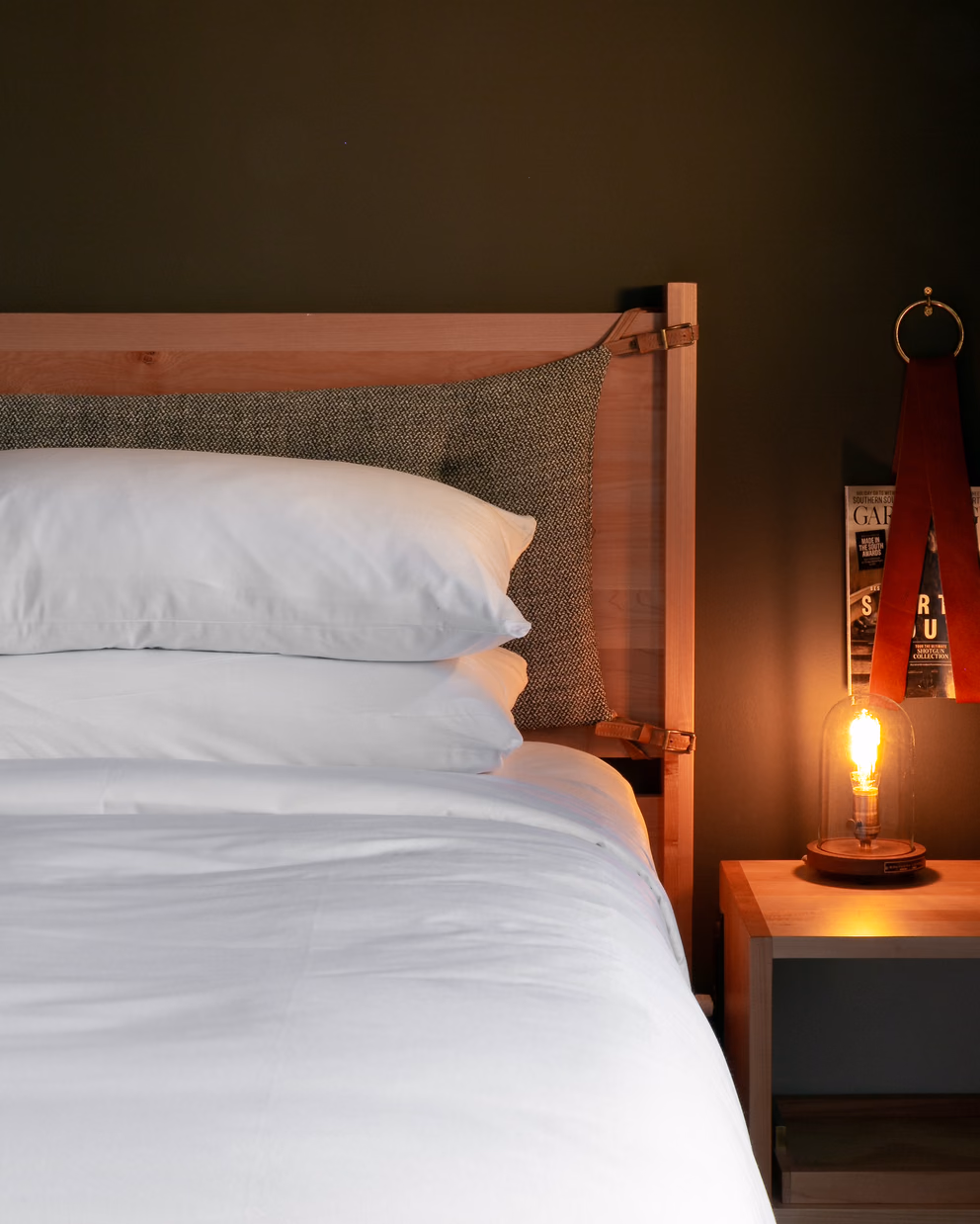 Bode Nashville bedroom with crisp white bedding, a wooden headboard, and an Edison bulb lamp