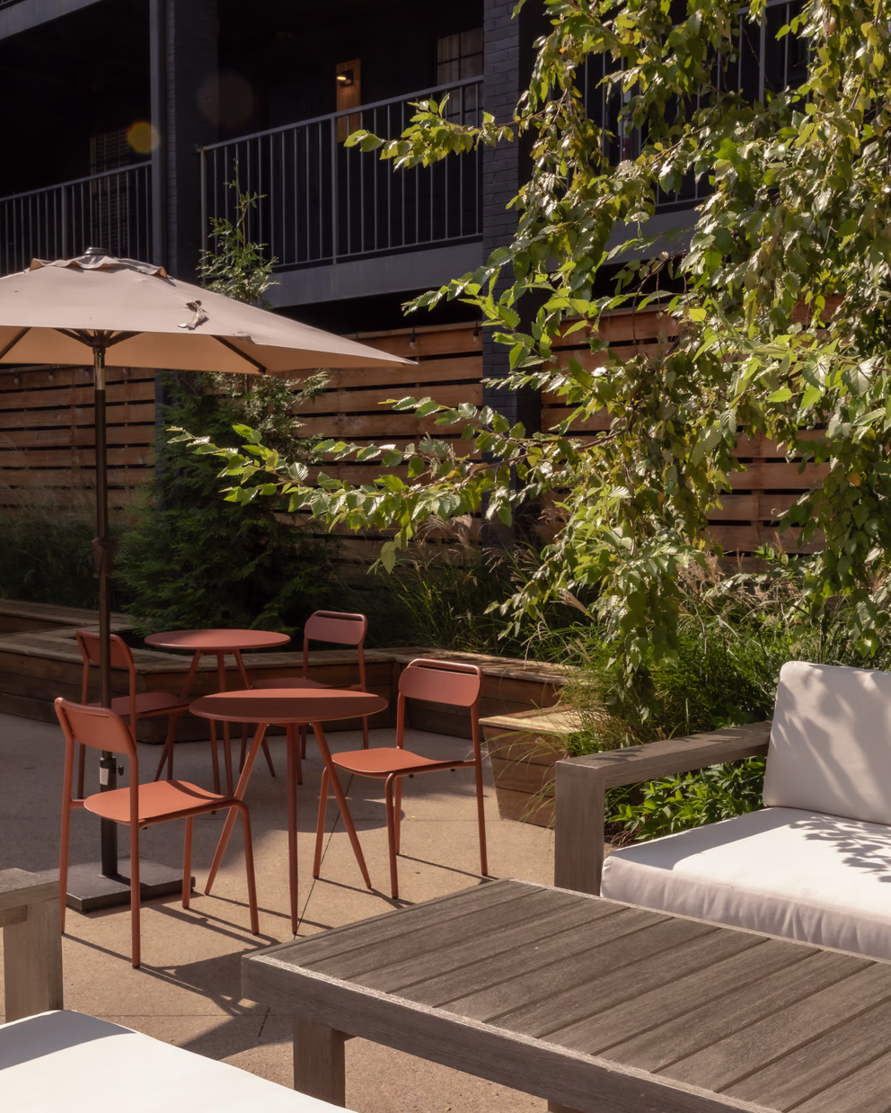Bode Nashville courtyard patio with orange bistro chairs, a market umbrella, and lush greenery