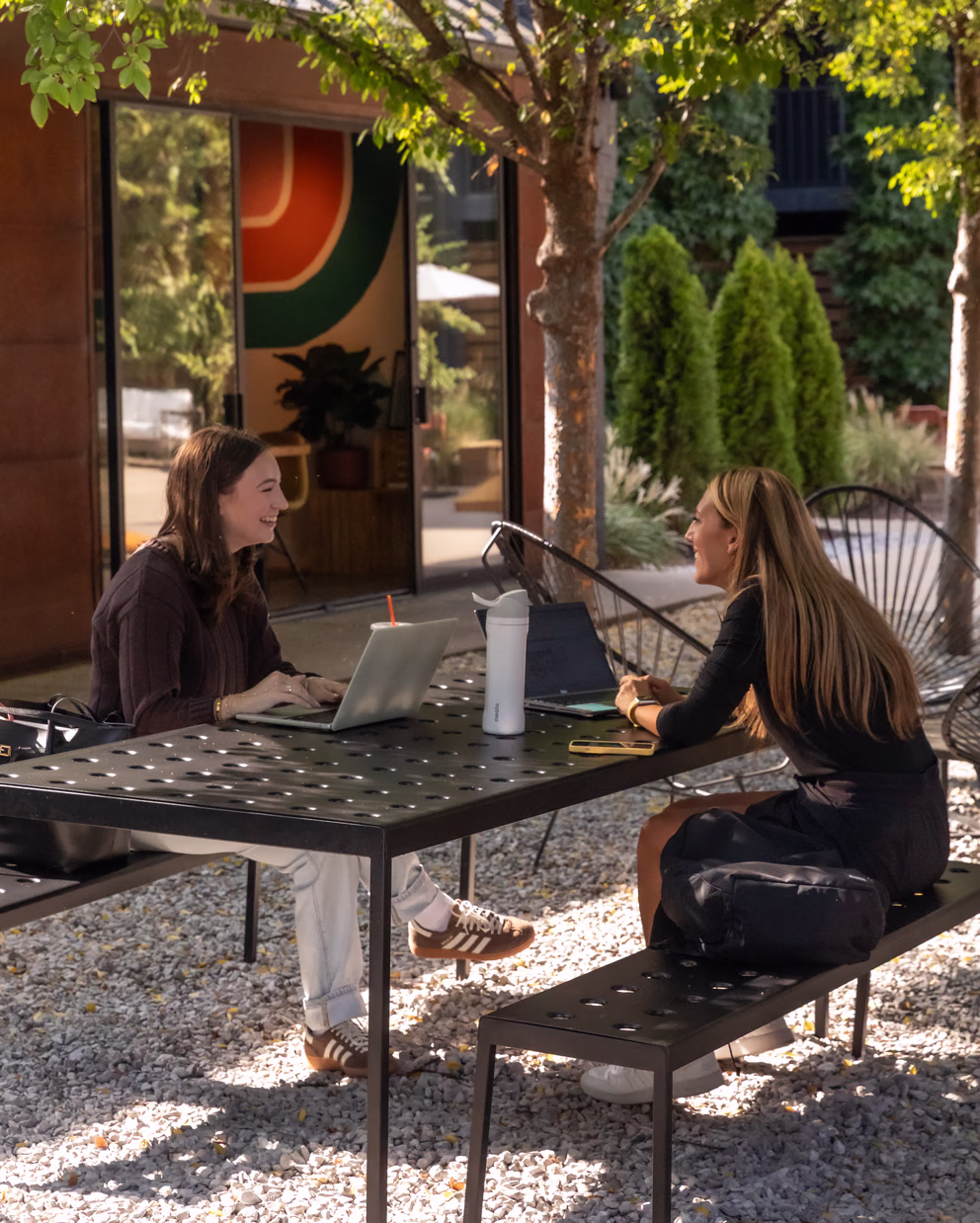 Two guests working on laptops at an outdoor table in the Bode Nashville courtyard near Dawn cafe