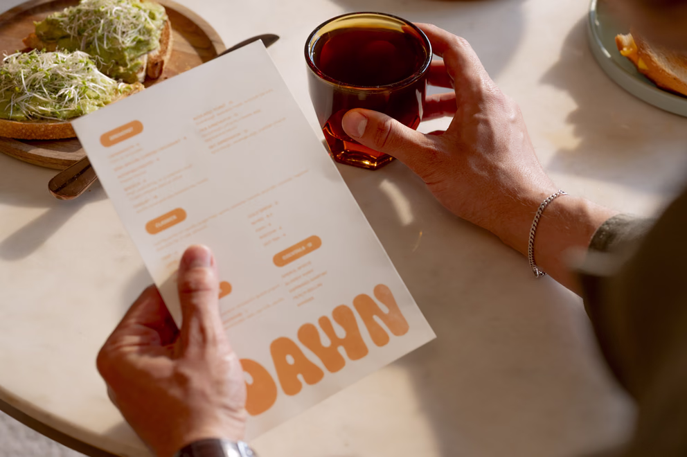 Guest reading the Dawn cafe menu while holding an iced tea beside avocado toast