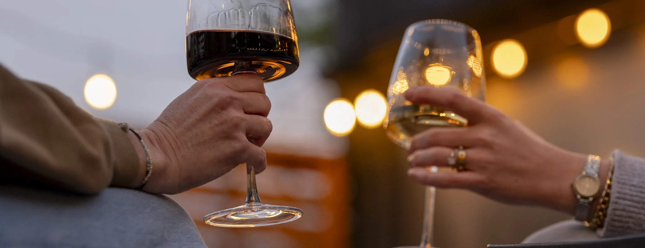 Two guests toasting with red and white wine under string lights at Bode Nashville