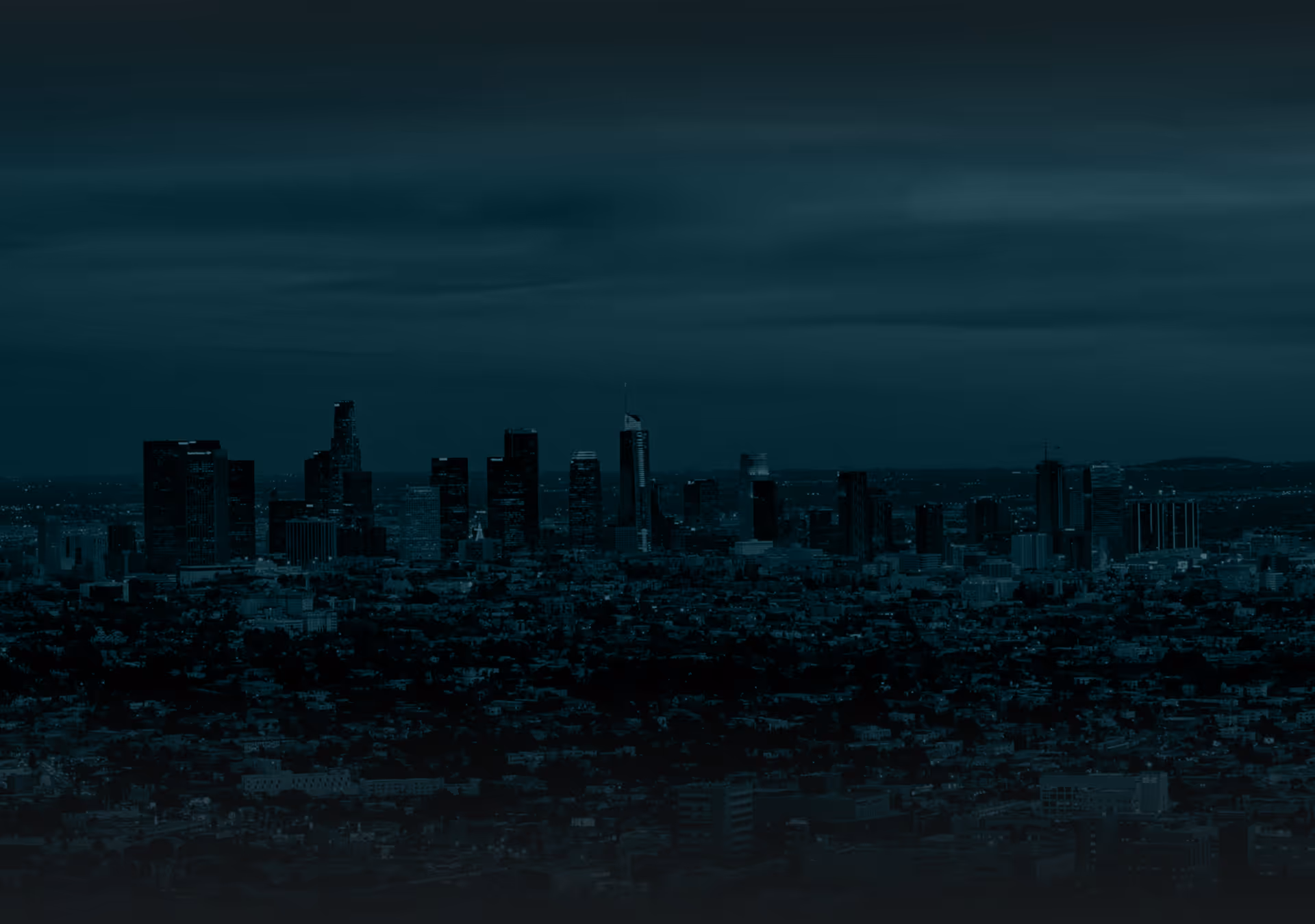 City skyline at dusk with tall buildings and a cloudy sky above.