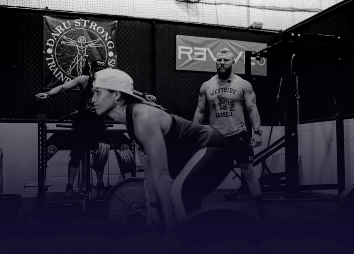 Woman weightlifting in a gym with a trainer standing nearby.