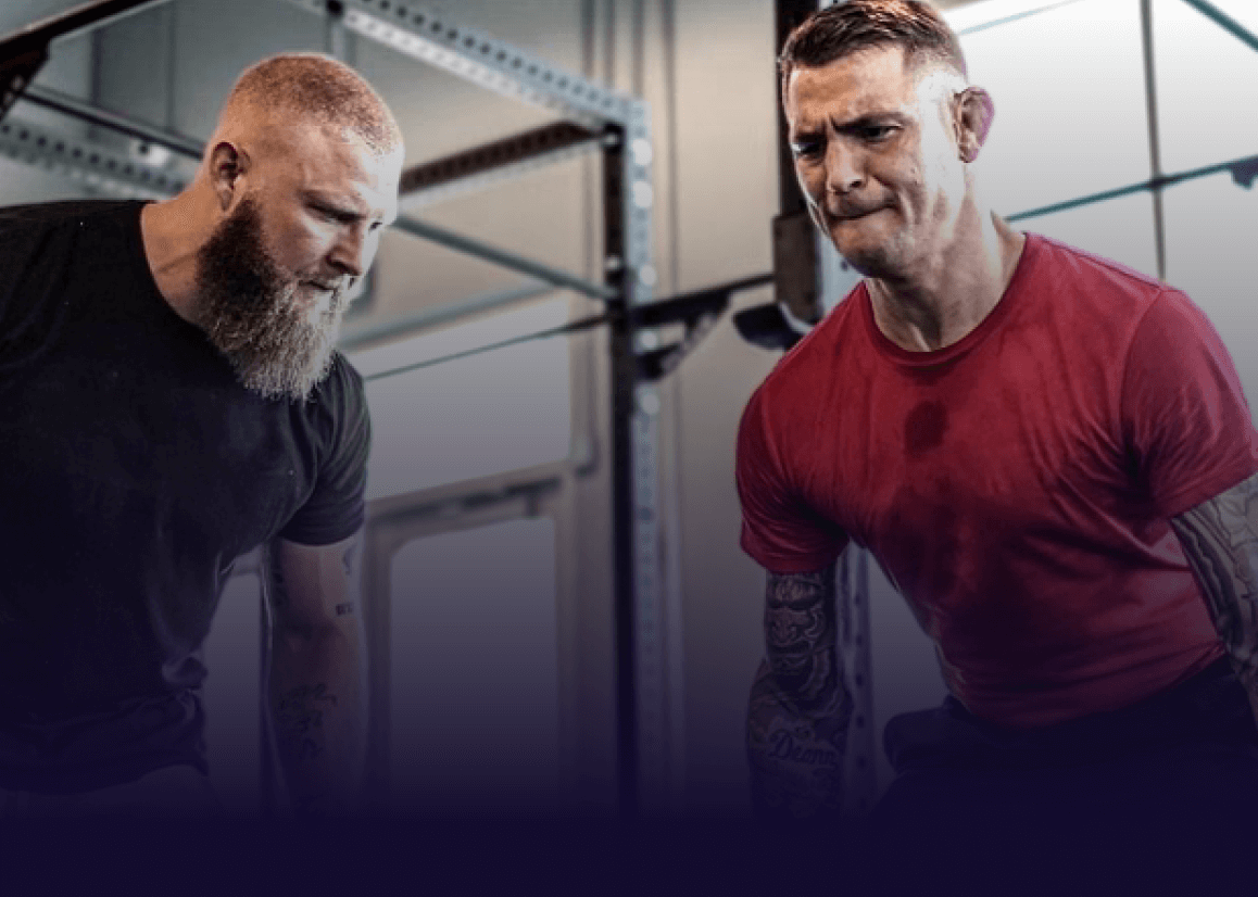 Man in a red Tshirt is lifting weights with a trainer. The strain is showing on his face.