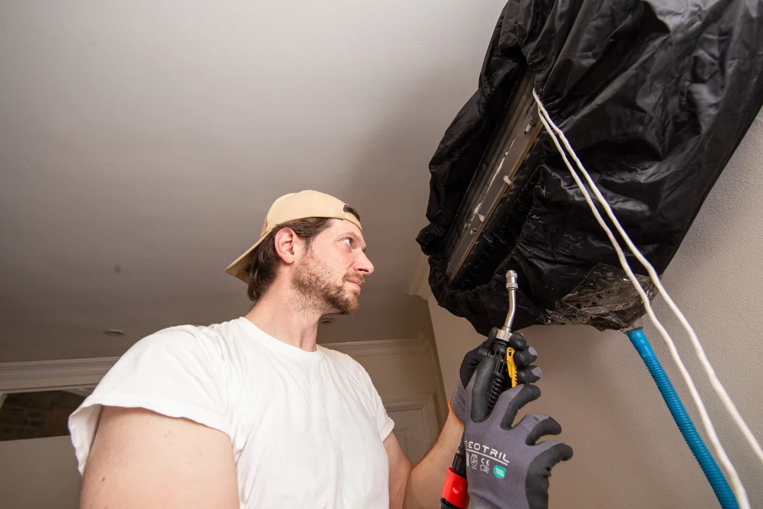 HVAC technician cleaning a ductless mini-split indoor unit to prevent clogged AC drain line issues