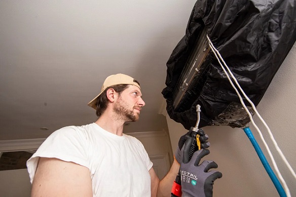 HVAC technician inspecting and cleaning a wall-mounted indoor air conditioning unit in a home