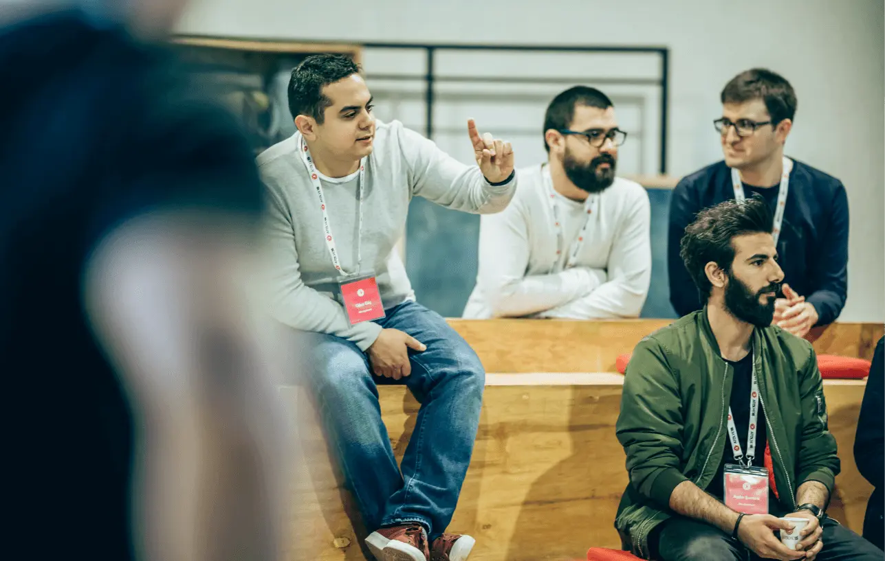 A small group in discussion at an event, with one participant gesturing while others listen attentively.
